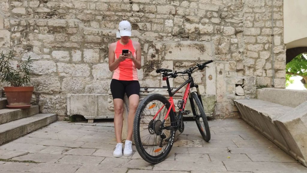 Biciklistica uz bicikl provjerava aplikaciju Bikademy na mobitelu